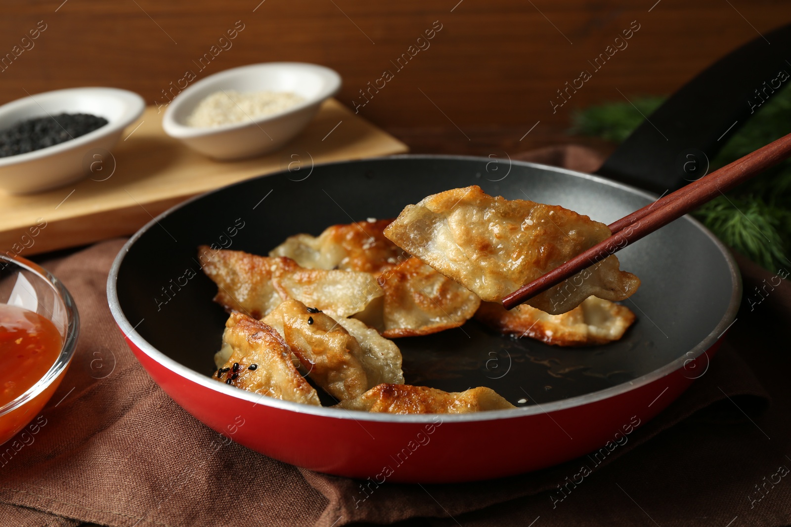 Photo of Taking tasty fried gyoza (dumpling) with chopsticks on table, closeup