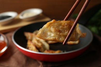 Photo of Holding tasty fried gyoza (dumpling) with chopsticks on table, closeup