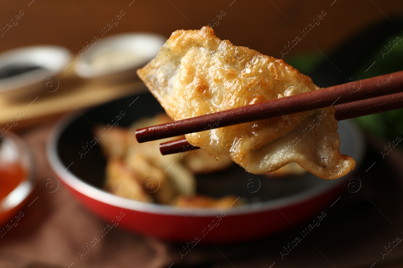 Photo of Holding tasty fried gyoza (dumpling) with chopsticks on table, closeup