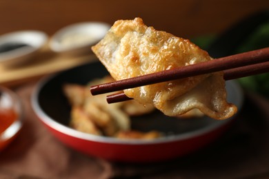 Photo of Holding tasty fried gyoza (dumpling) with chopsticks on table, closeup