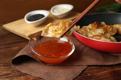 Photo of Dipping tasty fried gyoza (dumpling) into sauce on wooden table, closeup