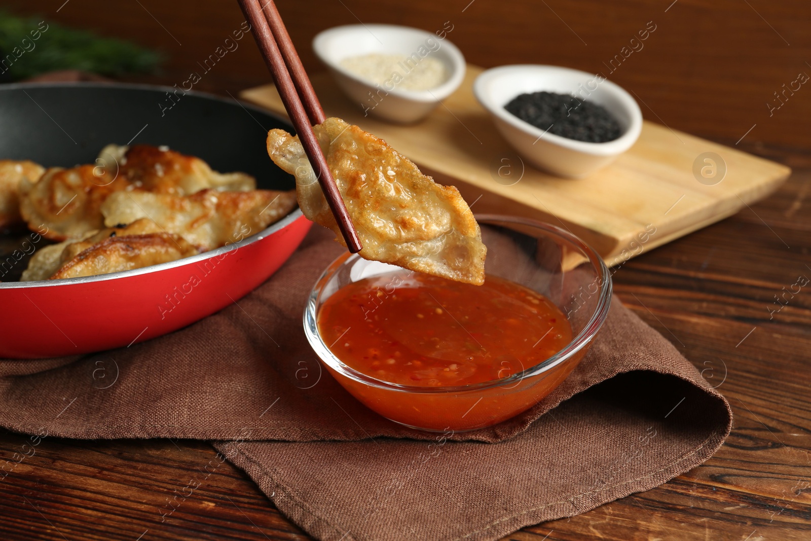 Photo of Dipping tasty fried gyoza (dumpling) into sauce on wooden table, closeup