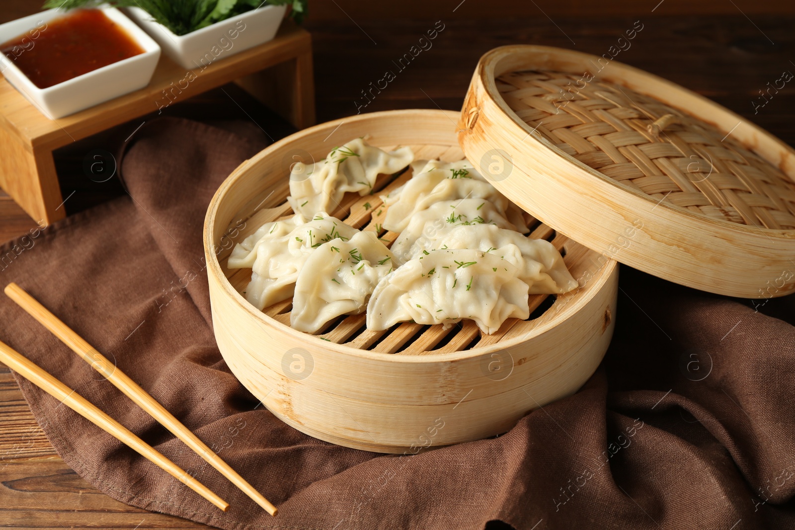 Photo of Tasty boiled gyoza (dumplings) in bamboo steamer and chopsticks on wooden table