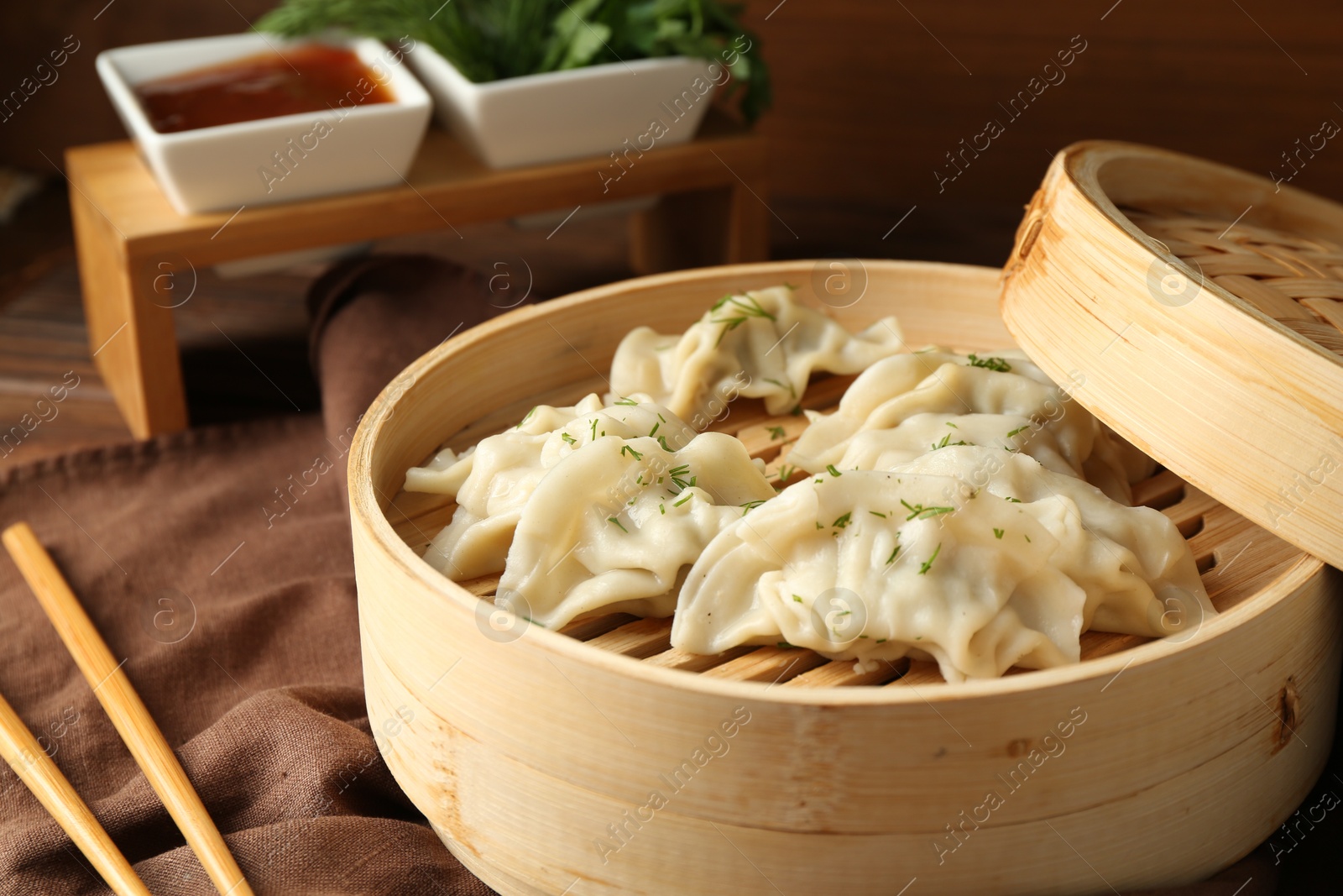 Photo of Tasty boiled gyoza (dumplings) in bamboo steamer and chopsticks on table, closeup