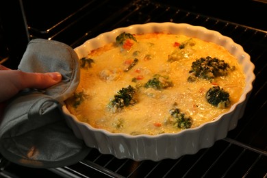 Photo of Woman taking delicious vegetable casserole out of oven, closeup