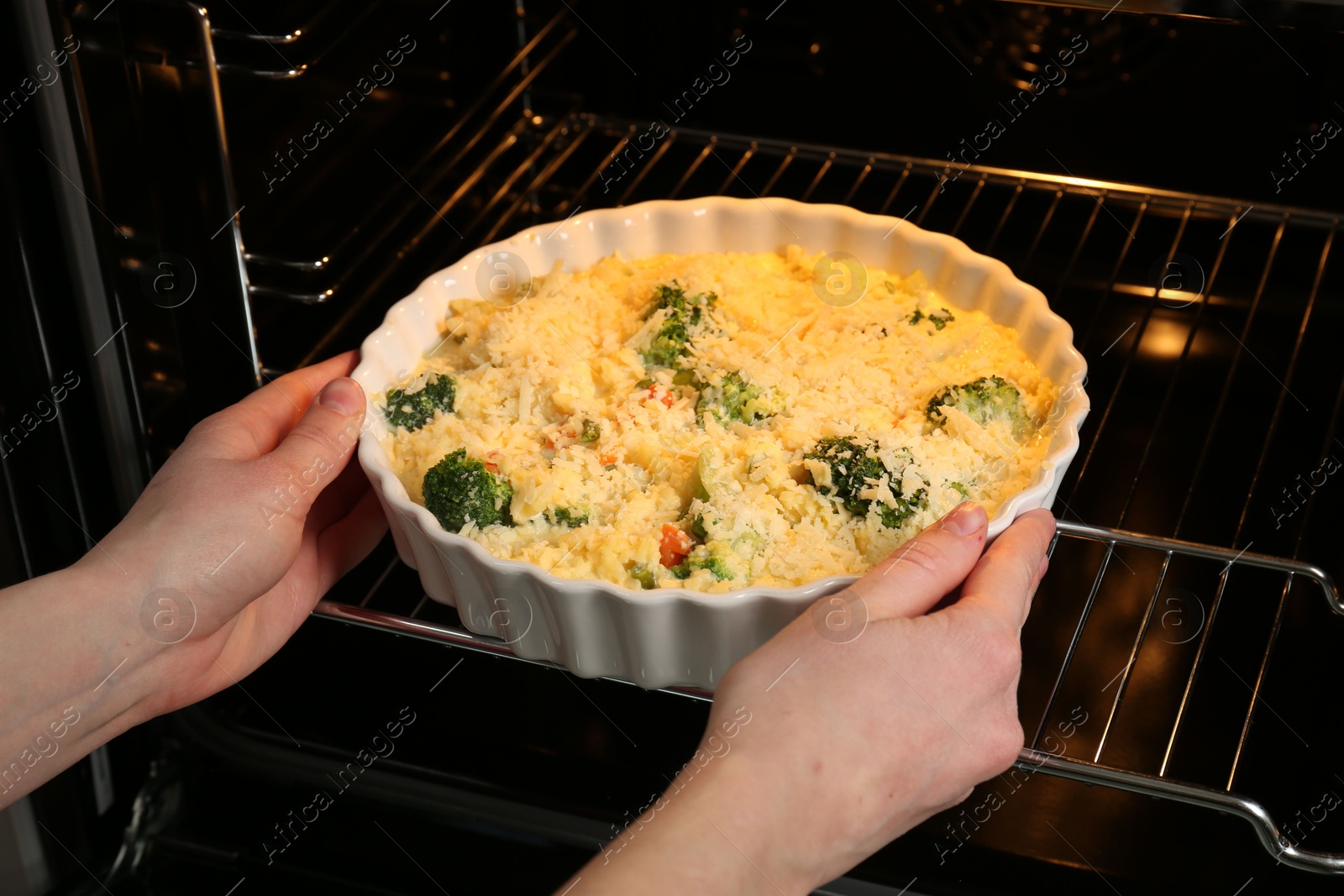 Photo of Woman putting uncooked vegetable casserole into oven, closeup