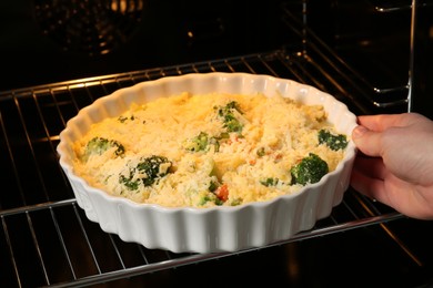 Photo of Woman putting uncooked vegetable casserole into oven, closeup