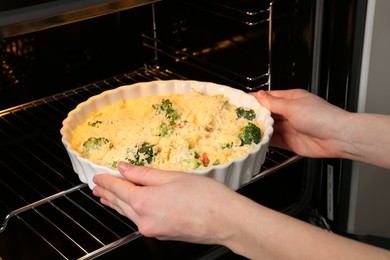 Photo of Woman putting uncooked vegetable casserole into oven, closeup