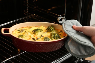 Photo of Woman taking delicious vegetable casserole out of oven, closeup