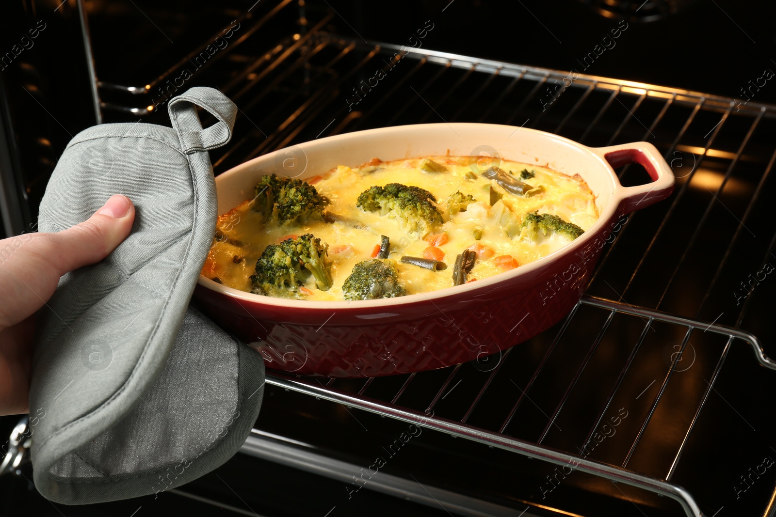 Photo of Woman taking delicious vegetable casserole out of oven, closeup