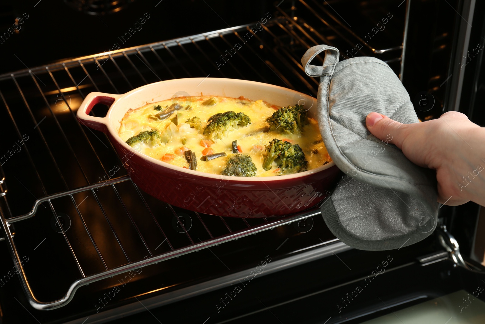 Photo of Woman taking delicious vegetable casserole out of oven, closeup