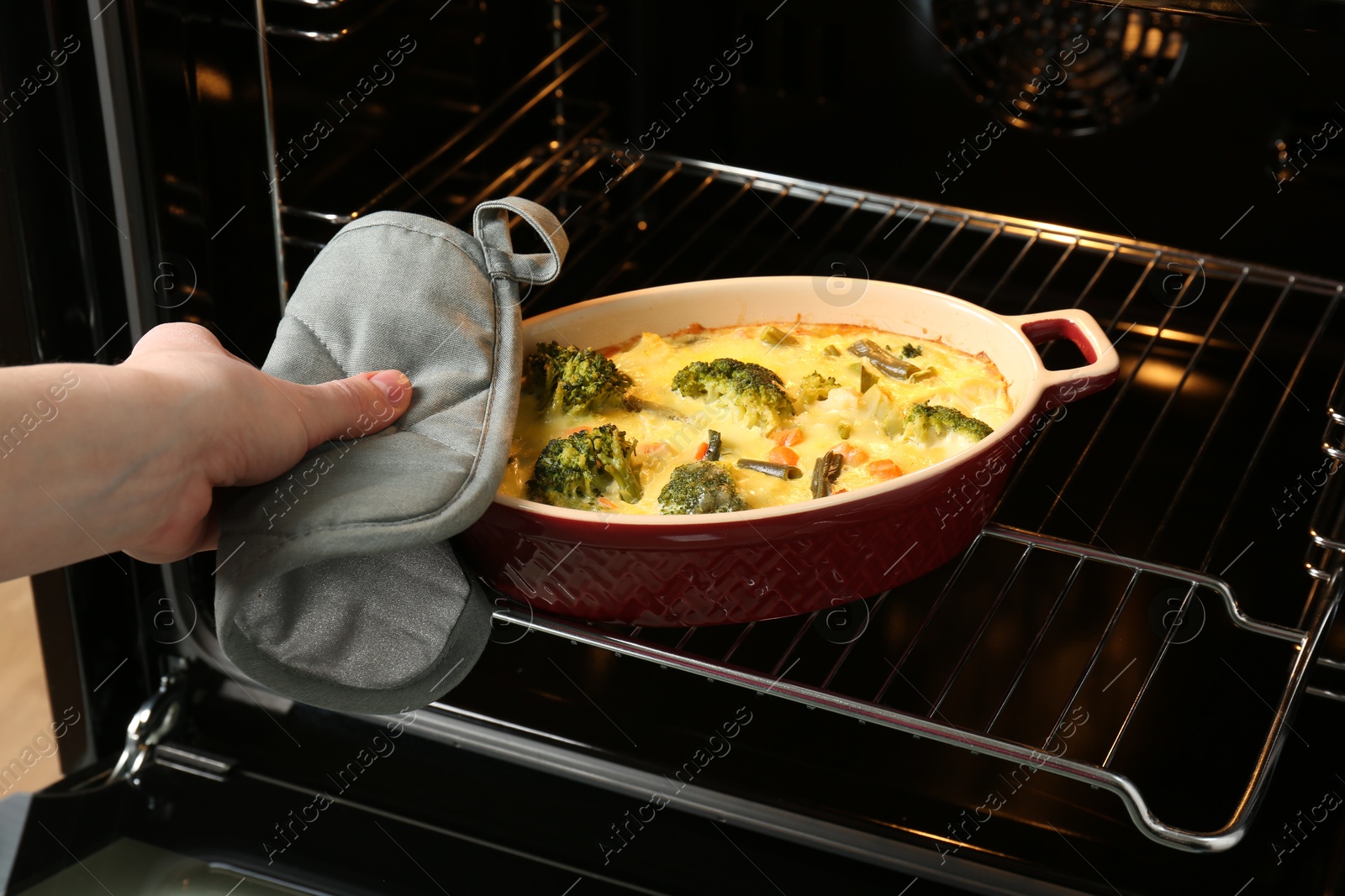 Photo of Woman taking delicious vegetable casserole out of oven, closeup