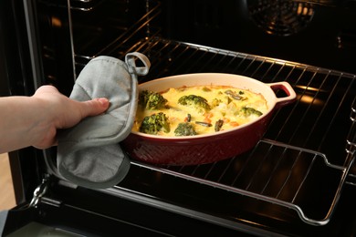 Photo of Woman taking delicious vegetable casserole out of oven, closeup