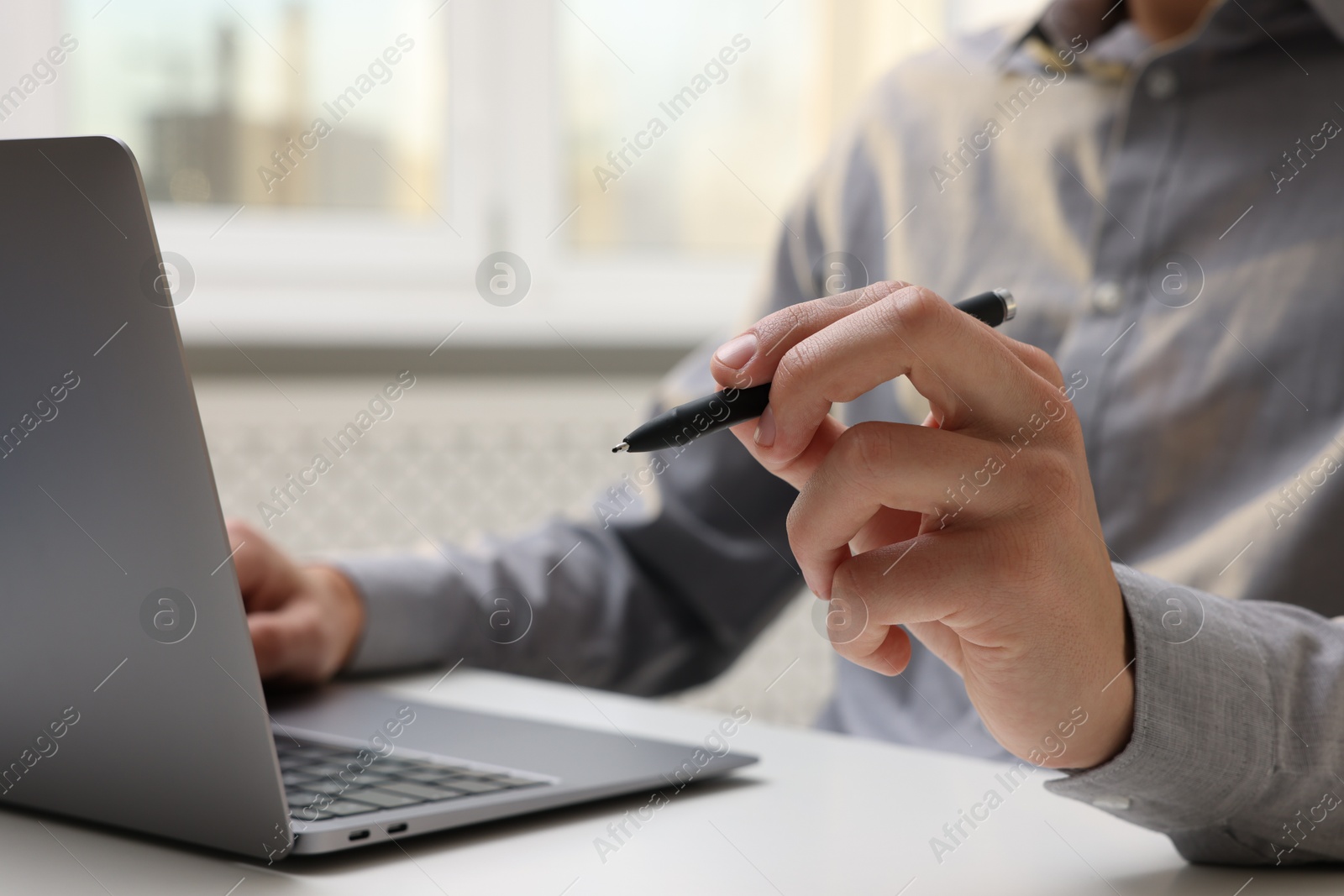 Photo of Electronic signature. Man with stylus and laptop at white table indoors, closeup