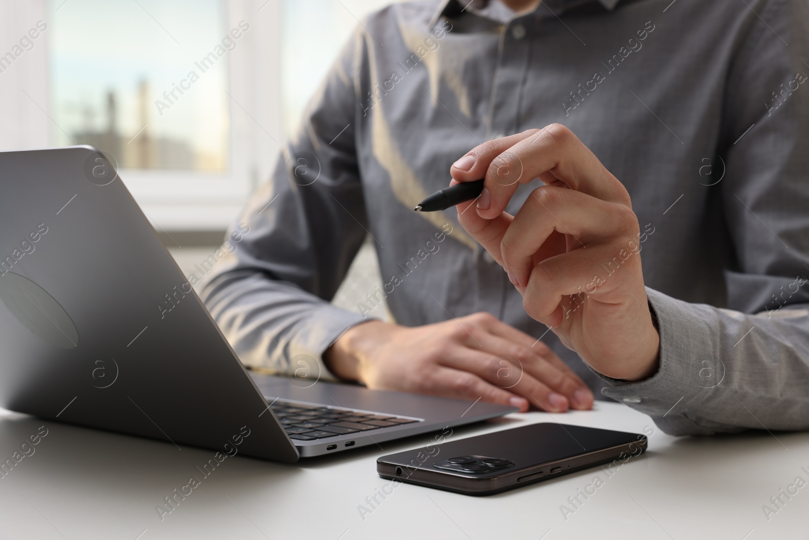 Photo of Electronic signature. Man with stylus, laptop and smartphone at white table indoors, closeup