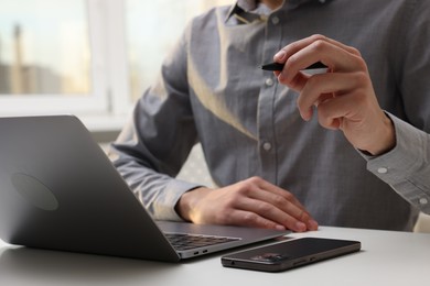 Photo of Electronic signature. Man with stylus, laptop and smartphone at white table indoors, closeup