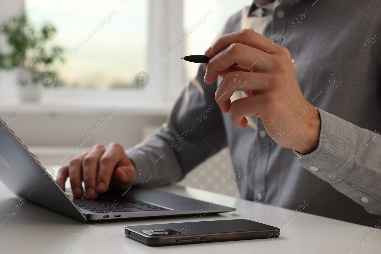 Photo of Electronic signature. Man with stylus, laptop and smartphone at white table indoors, closeup