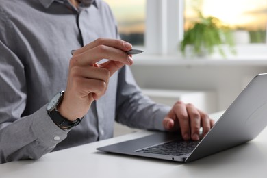 Photo of Electronic signature. Man with stylus and laptop at white table indoors, closeup