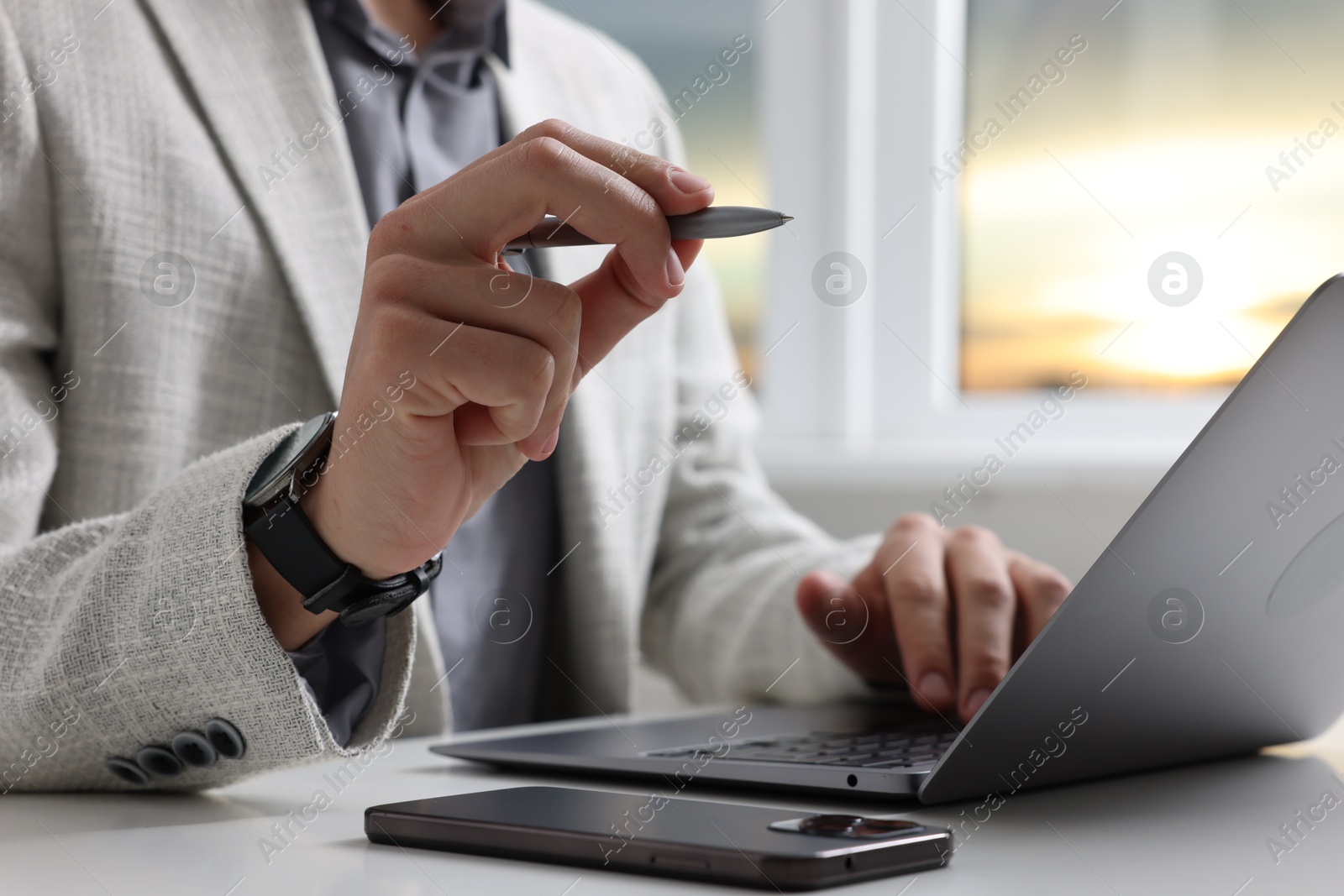 Photo of Electronic signature. Man with stylus, laptop and smartphone at white table indoors, closeup