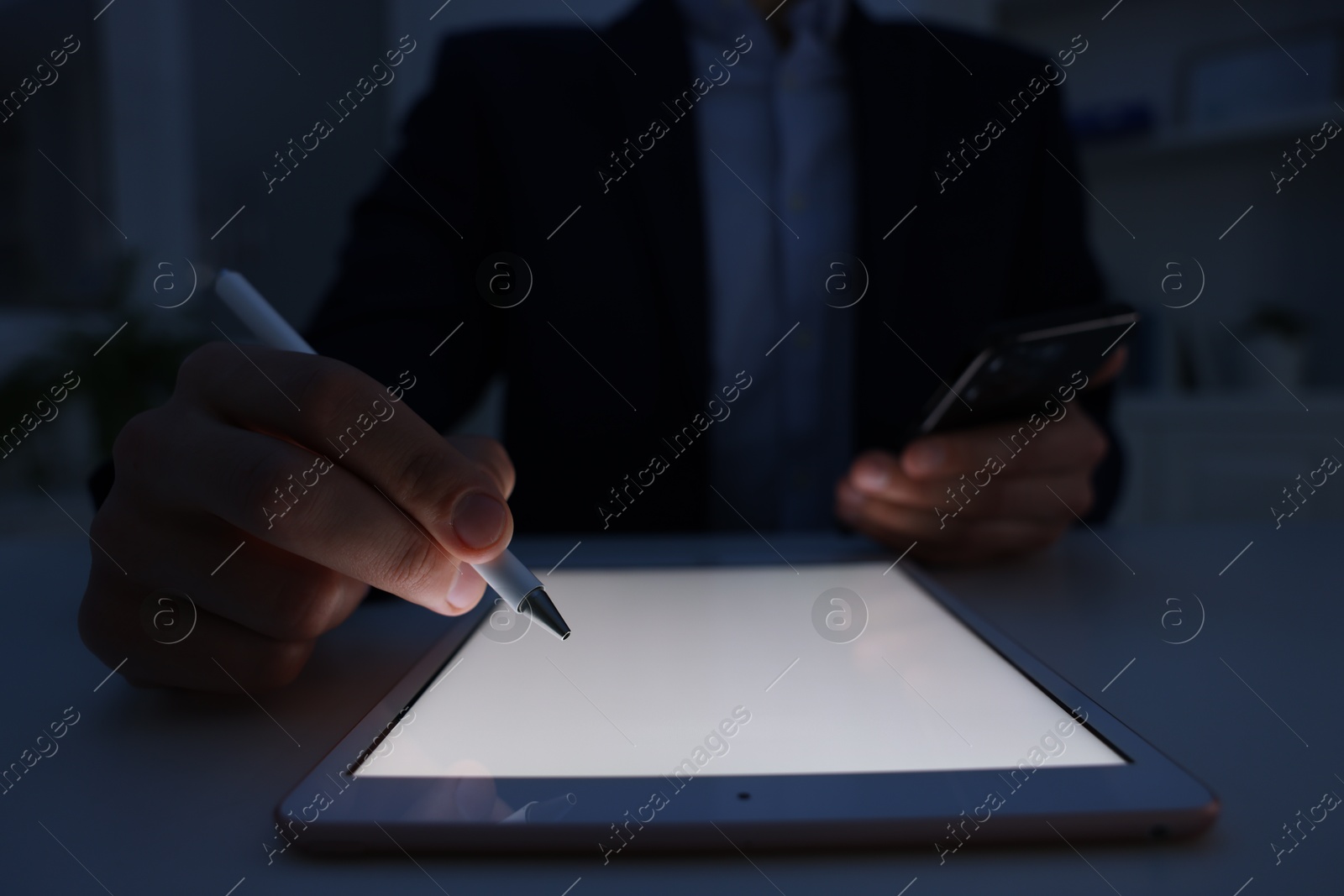 Photo of Electronic signature. Man with stylus, tablet and smartphone at table in dark office, closeup