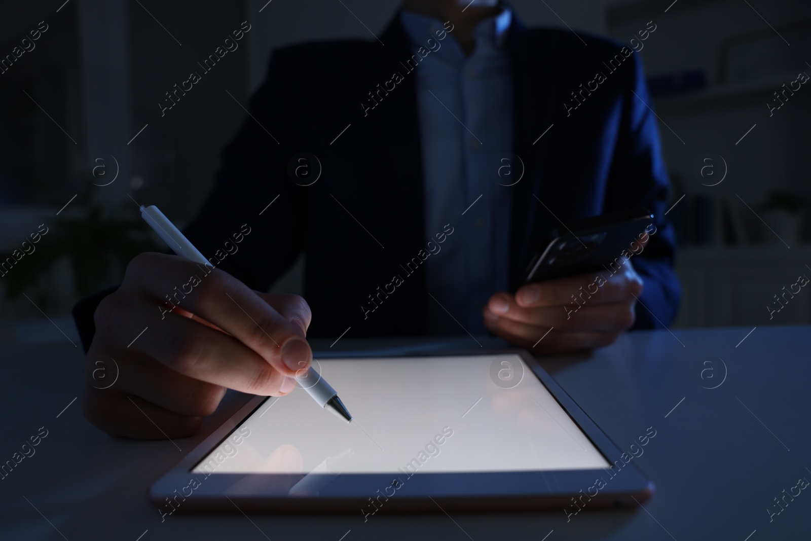 Photo of Electronic signature. Man with stylus, tablet and smartphone at table in dark office, closeup