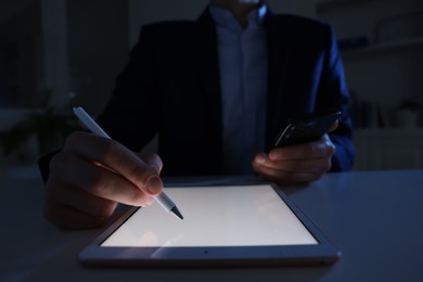 Photo of Electronic signature. Man with stylus, tablet and smartphone at table in dark office, closeup