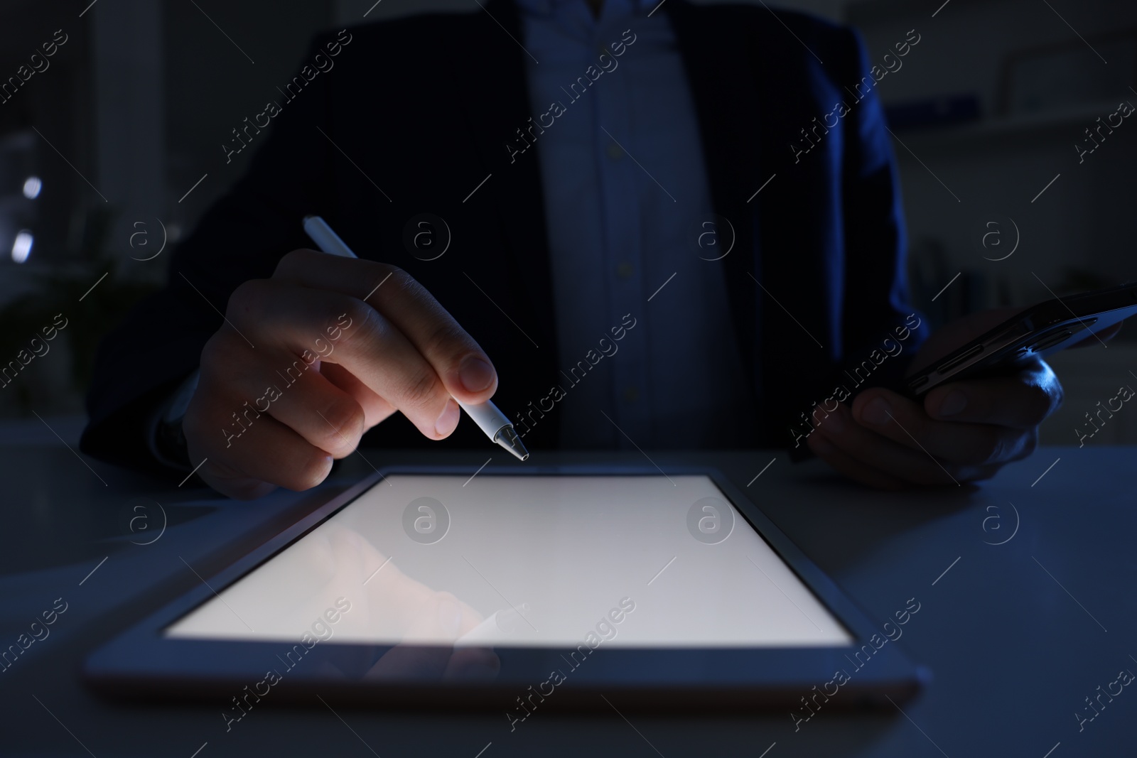 Photo of Electronic signature. Man with stylus, tablet and smartphone at table in dark office, closeup