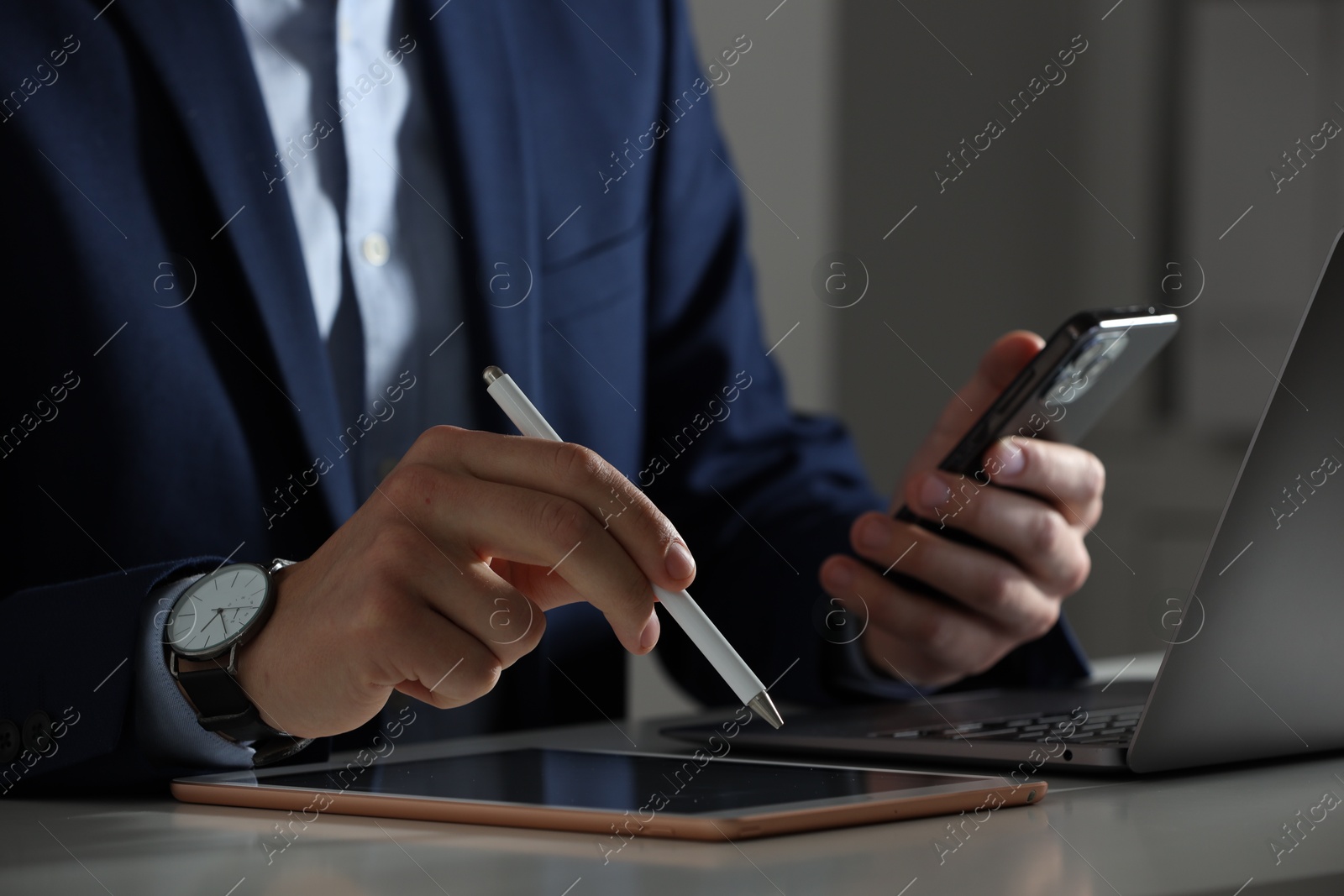 Photo of Electronic signature. Man with stylus, tablet, laptop and smartphone at table indoors, closeup