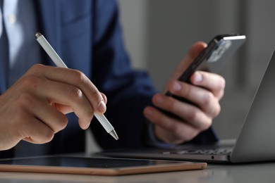 Photo of Electronic signature. Man with stylus, tablet, laptop and smartphone at table indoors, closeup