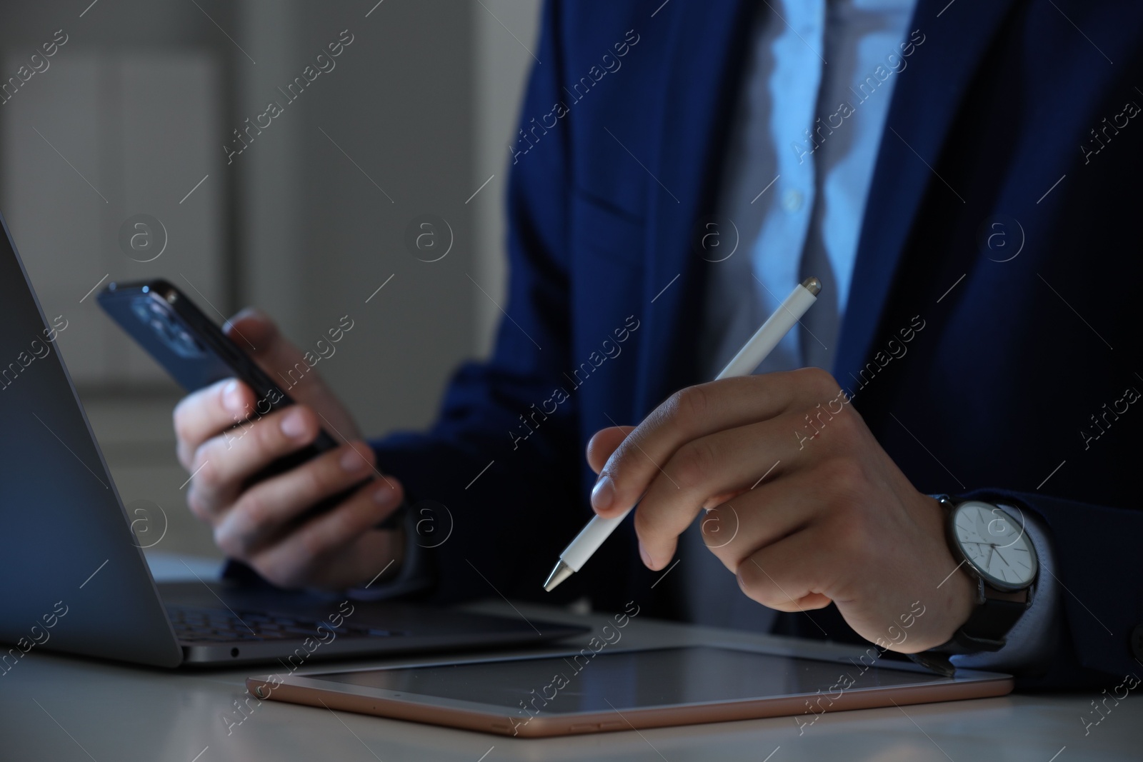 Photo of Electronic signature. Man with stylus, tablet, laptop and smartphone at table indoors, closeup