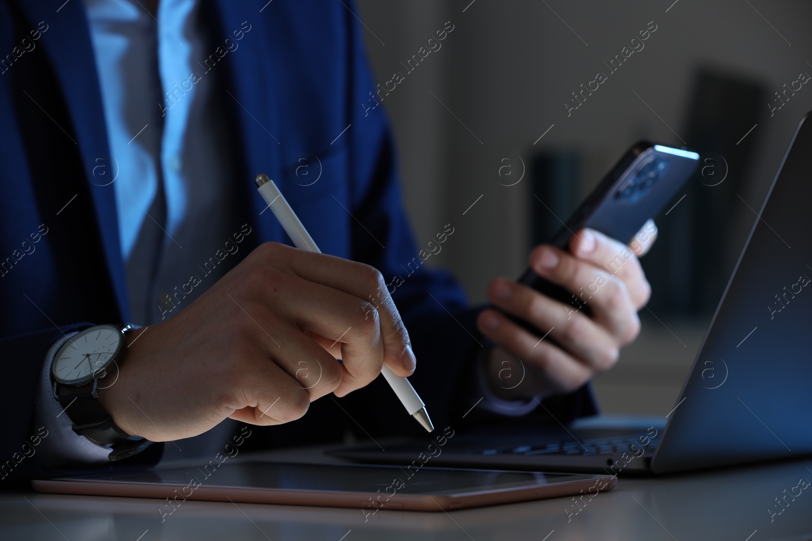 Photo of Electronic signature. Man with stylus, tablet, laptop and smartphone at table indoors, closeup