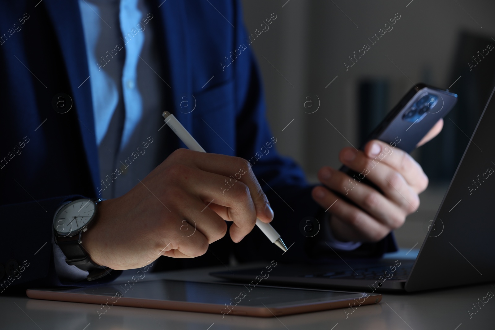 Photo of Electronic signature. Man with stylus, tablet, laptop and smartphone at table indoors, closeup