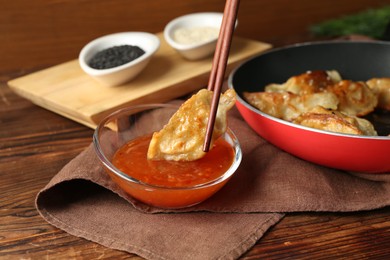 Photo of Dipping tasty fried gyoza (dumpling) into sauce on wooden table, closeup