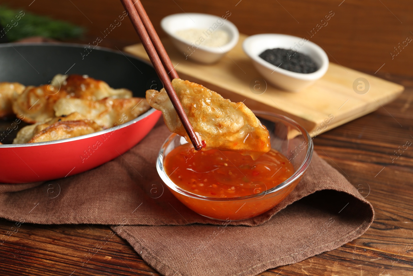 Photo of Dipping tasty fried gyoza (dumpling) into sauce on wooden table, closeup