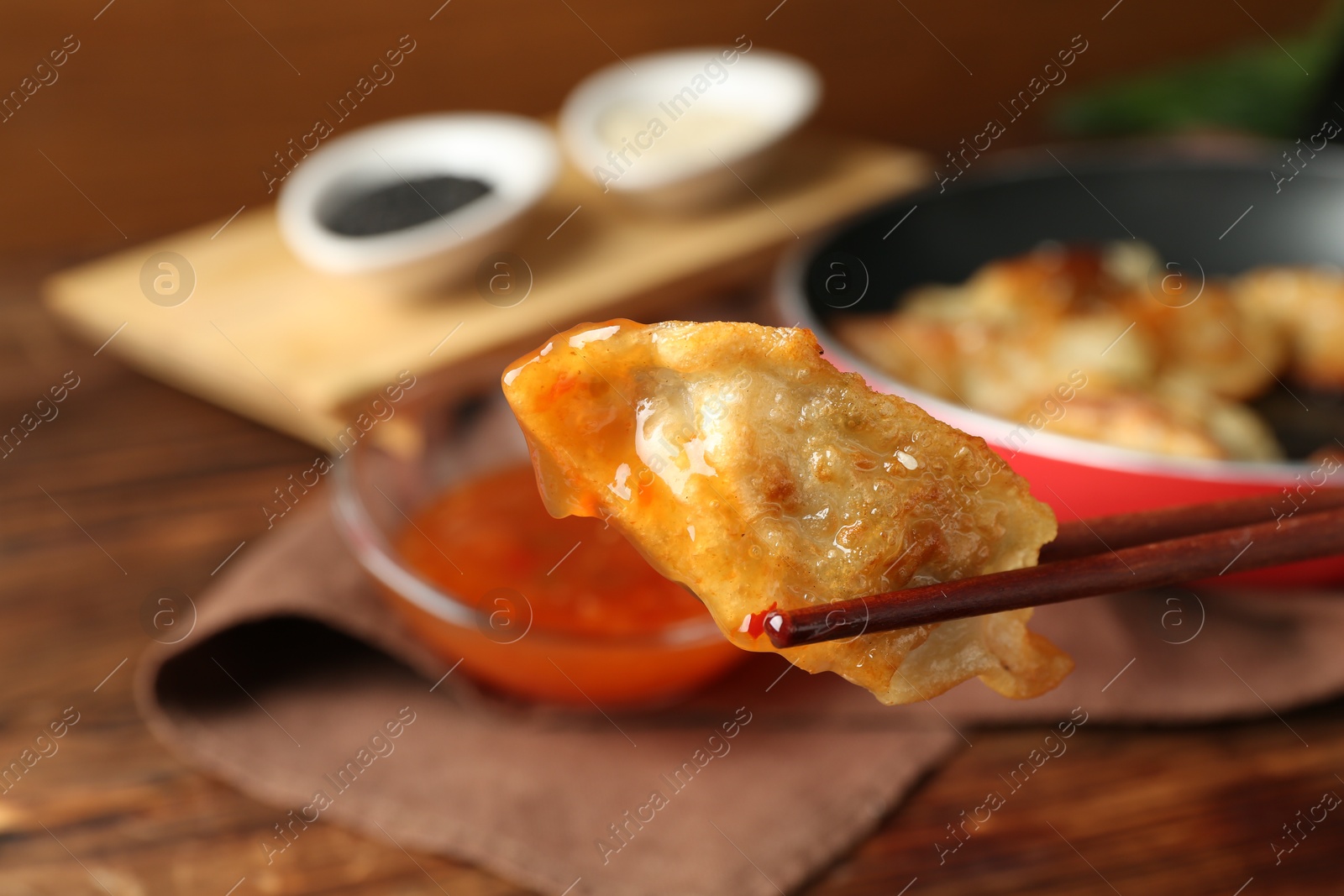 Photo of Dipping tasty fried gyoza (dumpling) into sauce on wooden table, closeup