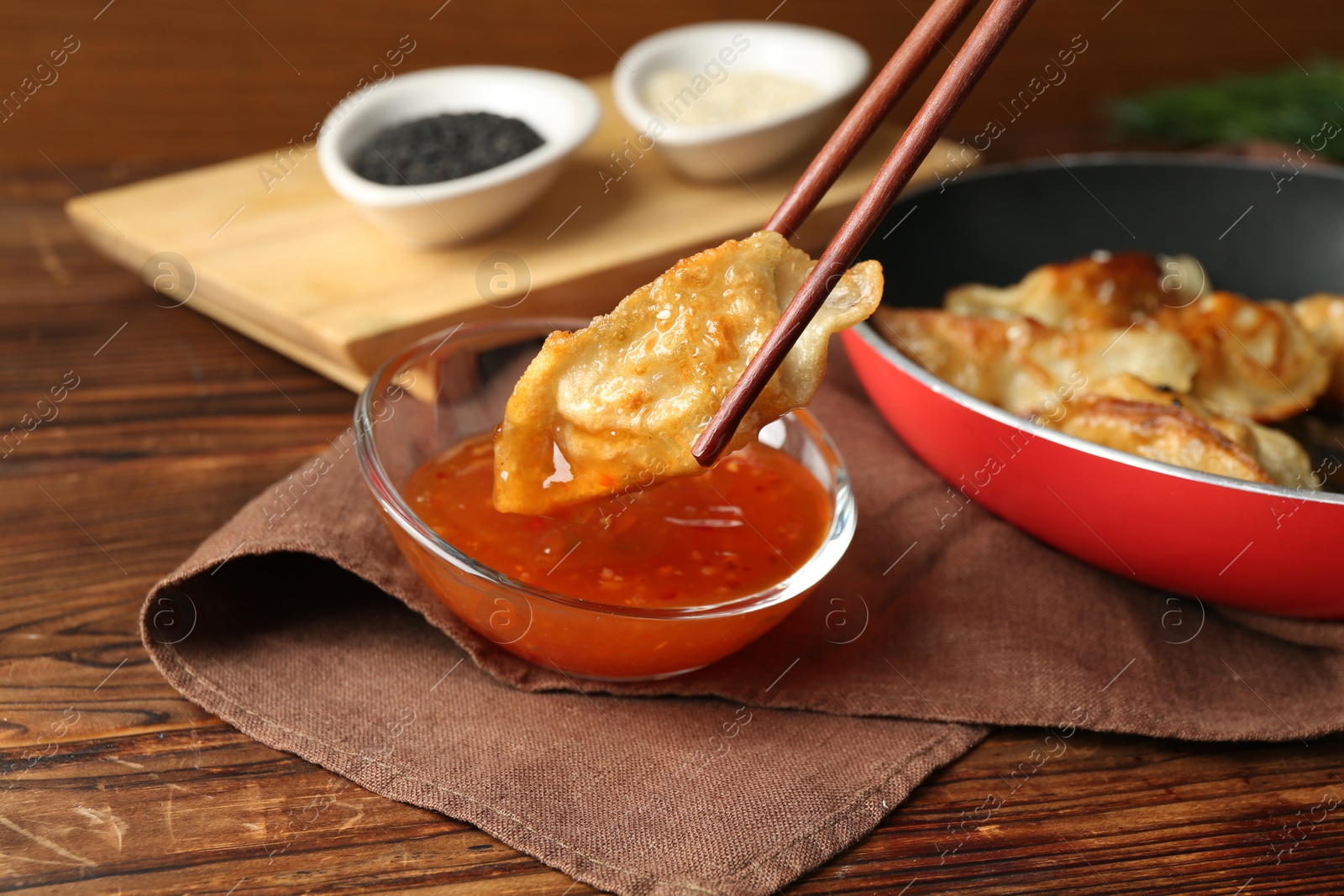 Photo of Dipping tasty fried gyoza (dumpling) into sauce on wooden table, closeup