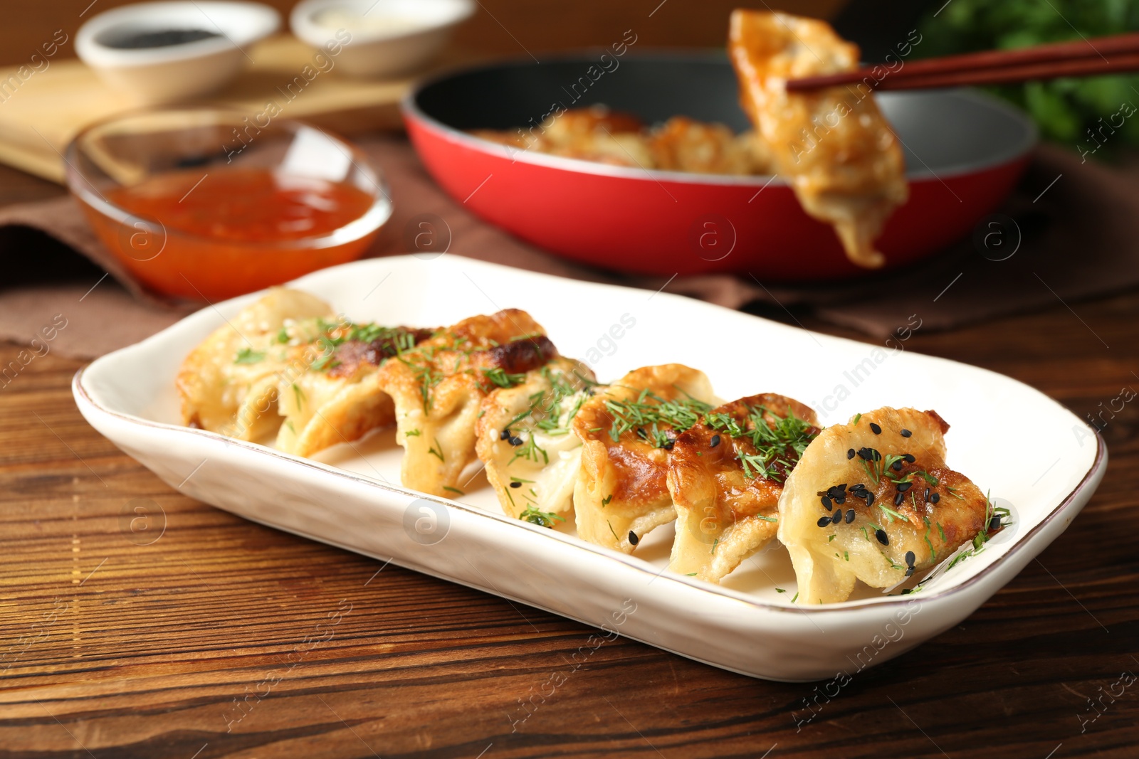 Photo of Taking tasty fried gyoza (dumpling) with chopsticks on wooden table, closeup