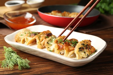 Photo of Taking tasty fried gyoza (dumpling) with chopsticks on wooden table, closeup