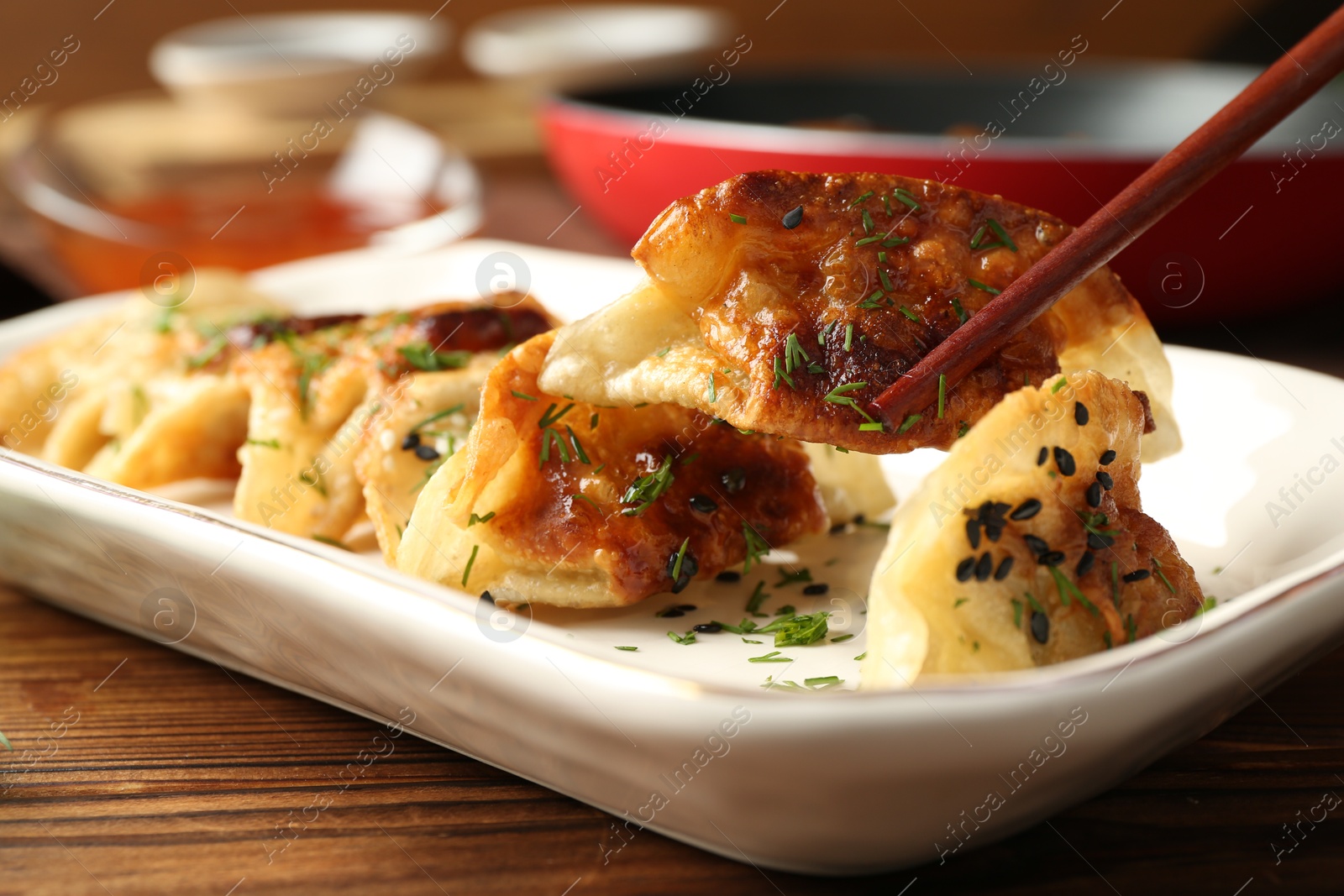 Photo of Taking tasty fried gyoza (dumpling) with chopsticks on wooden table, closeup