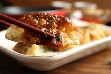 Photo of Taking tasty fried gyoza (dumpling) with chopsticks on wooden table, closeup