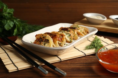 Photo of Tasty fried gyoza (dumplings), chopsticks and sauce on wooden table