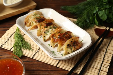 Photo of Tasty fried gyoza (dumplings), chopsticks and sauce on wooden table