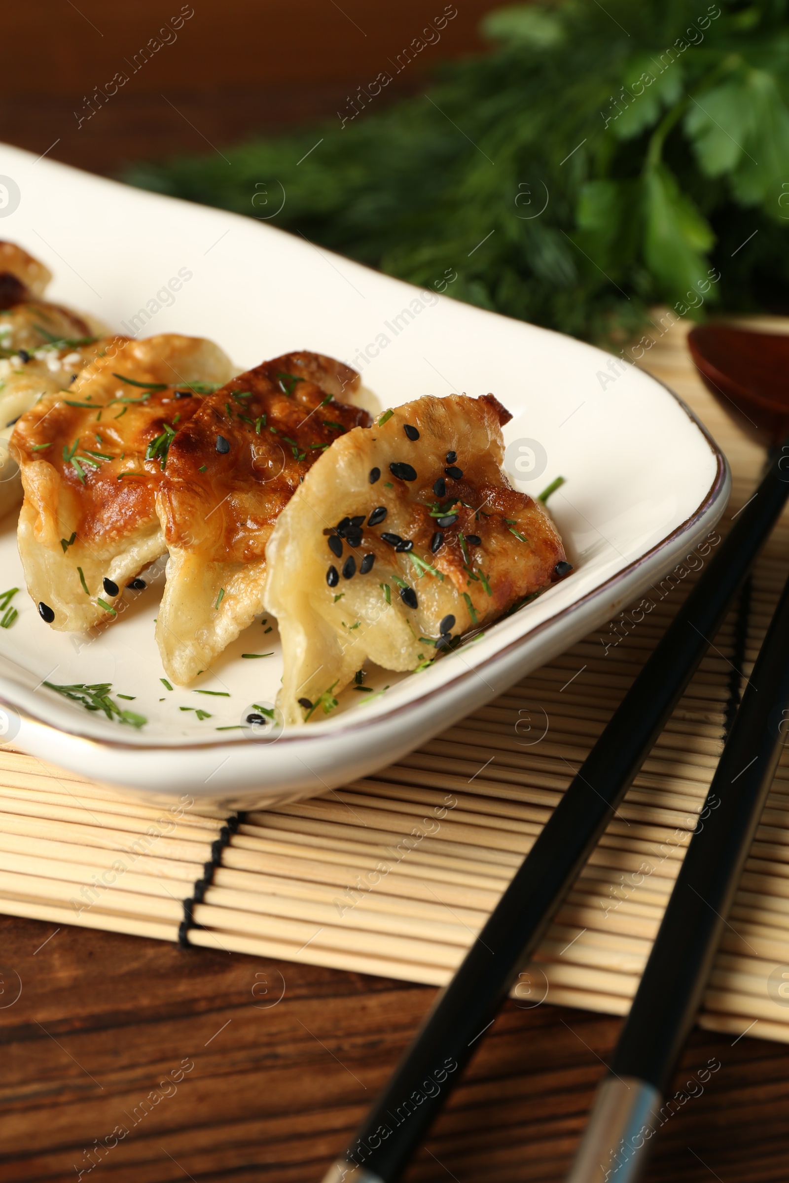 Photo of Tasty fried gyoza (dumplings) and chopsticks on wooden table, closeup