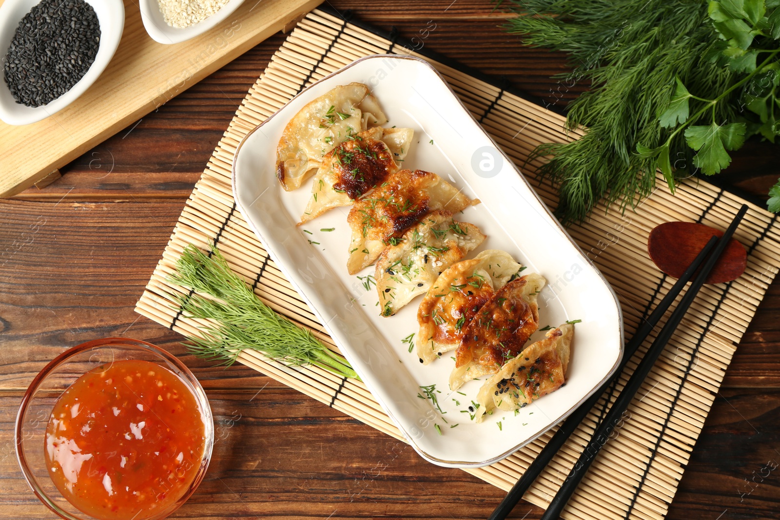 Photo of Tasty fried gyoza (dumplings), chopsticks and sauce on wooden table, flat lay