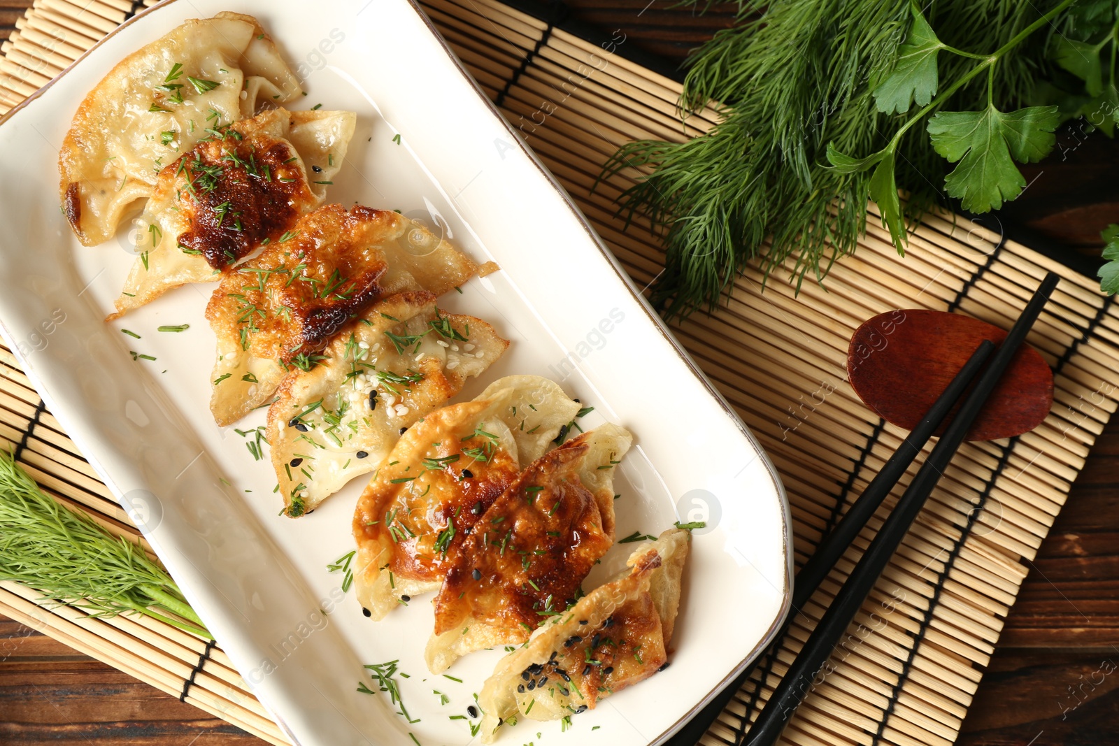 Photo of Tasty fried gyoza (dumplings) and chopsticks on wooden table, flat lay