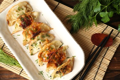 Photo of Tasty fried gyoza (dumplings) and chopsticks on wooden table, flat lay