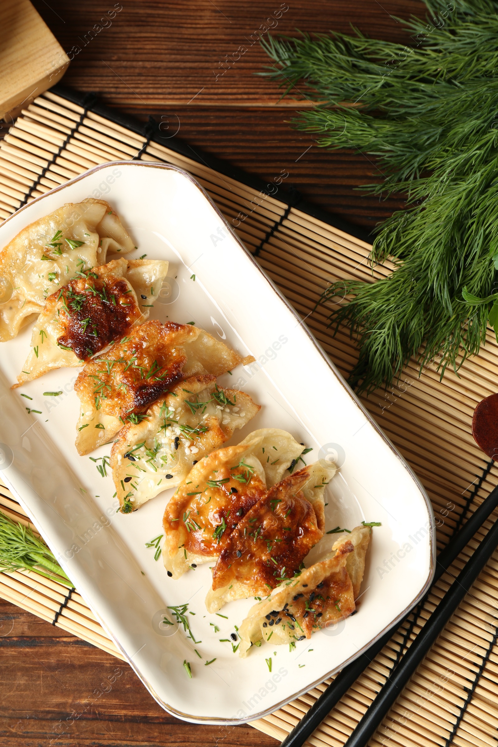 Photo of Tasty fried gyoza (dumplings) and chopsticks on wooden table, flat lay