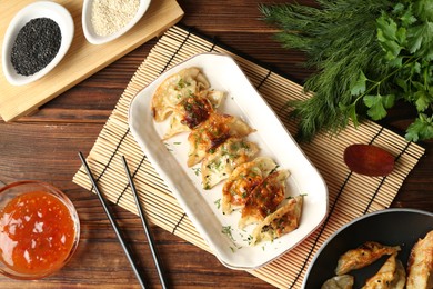 Photo of Tasty fried gyoza (dumplings), chopsticks and sauce on wooden table, flat lay