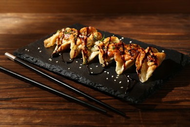 Photo of Tasty fried gyoza (dumplings) and chopsticks on wooden table, closeup