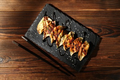 Photo of Tasty fried gyoza (dumplings) and chopsticks on wooden table, top view